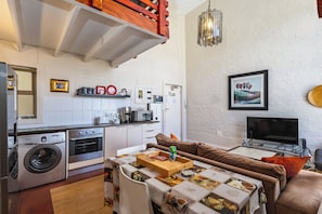 A compact living space with a kitchenette, a dining area with a table set for two, a sofa, and a flat-screen TV.