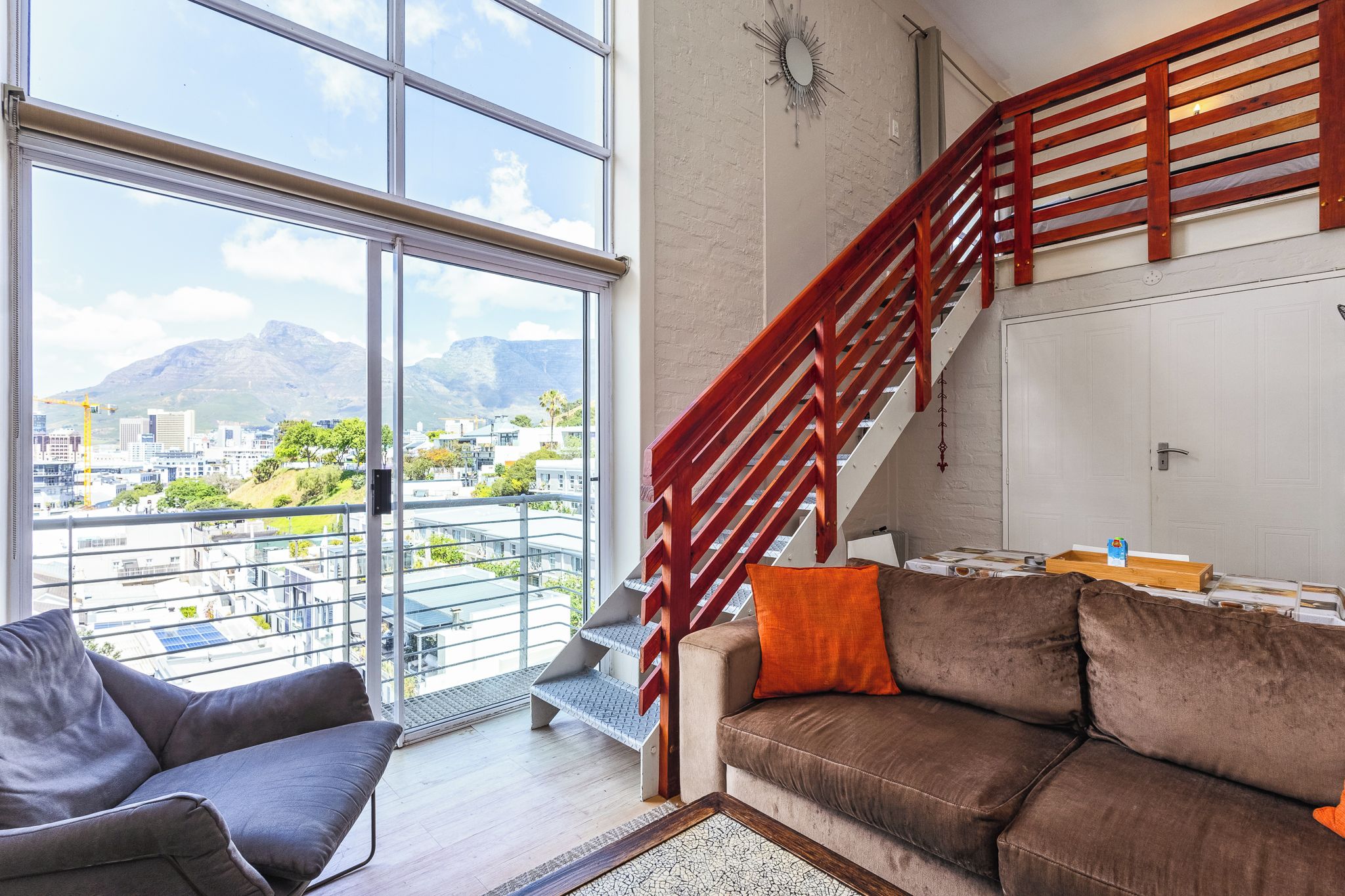 A spacious living area with a large window, a wooden staircase, and a sofa with cushions.