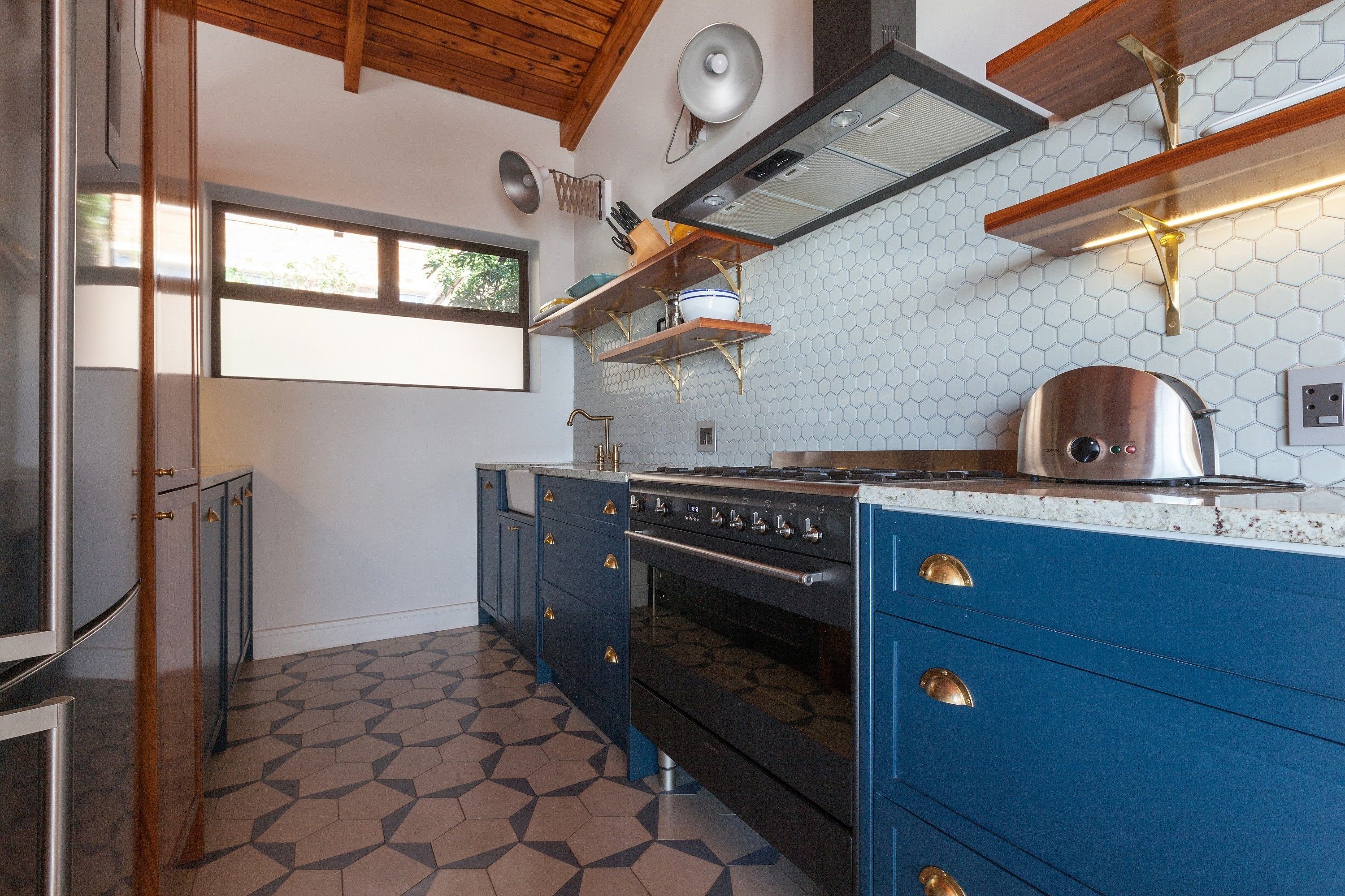 A kitchen with a modern stove, blue cabinets, and a geometric tile floor.