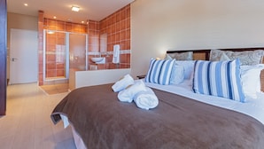 A modern hotel room with a large bed, a bathroom with a glass shower enclosure, and a white sink.