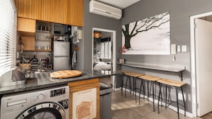 Une cuisine compacte avec des meubles en bois, un lave-linge encastré, une planche à découper en bois et un coin bar avec des tabourets.