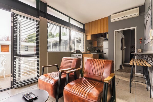 A modern kitchen with a built-in oven, a dining area with two leather chairs, and a bar stool.