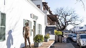 Une rue bordée de voitures garées, une statue et un bâtiment avec des volets.
