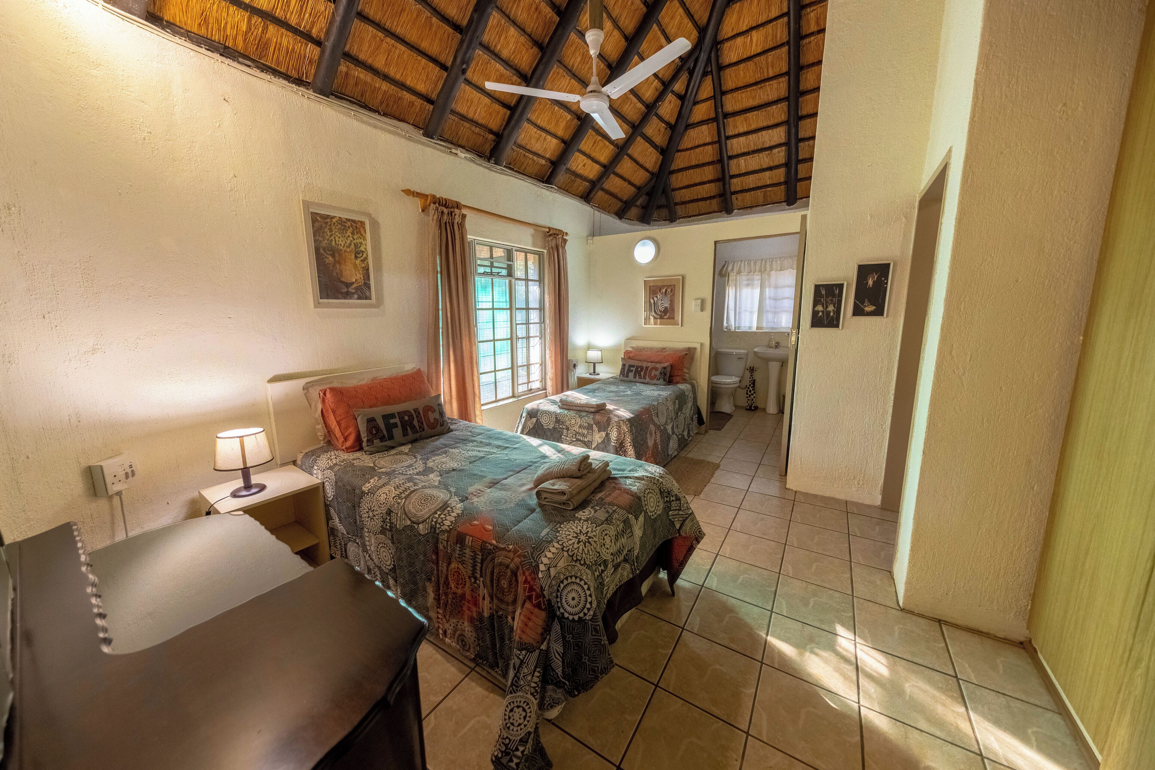 A room with two beds, a ceiling fan, and a window with curtains.