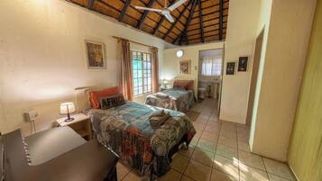 A room with two beds, a ceiling fan, and a window with curtains.