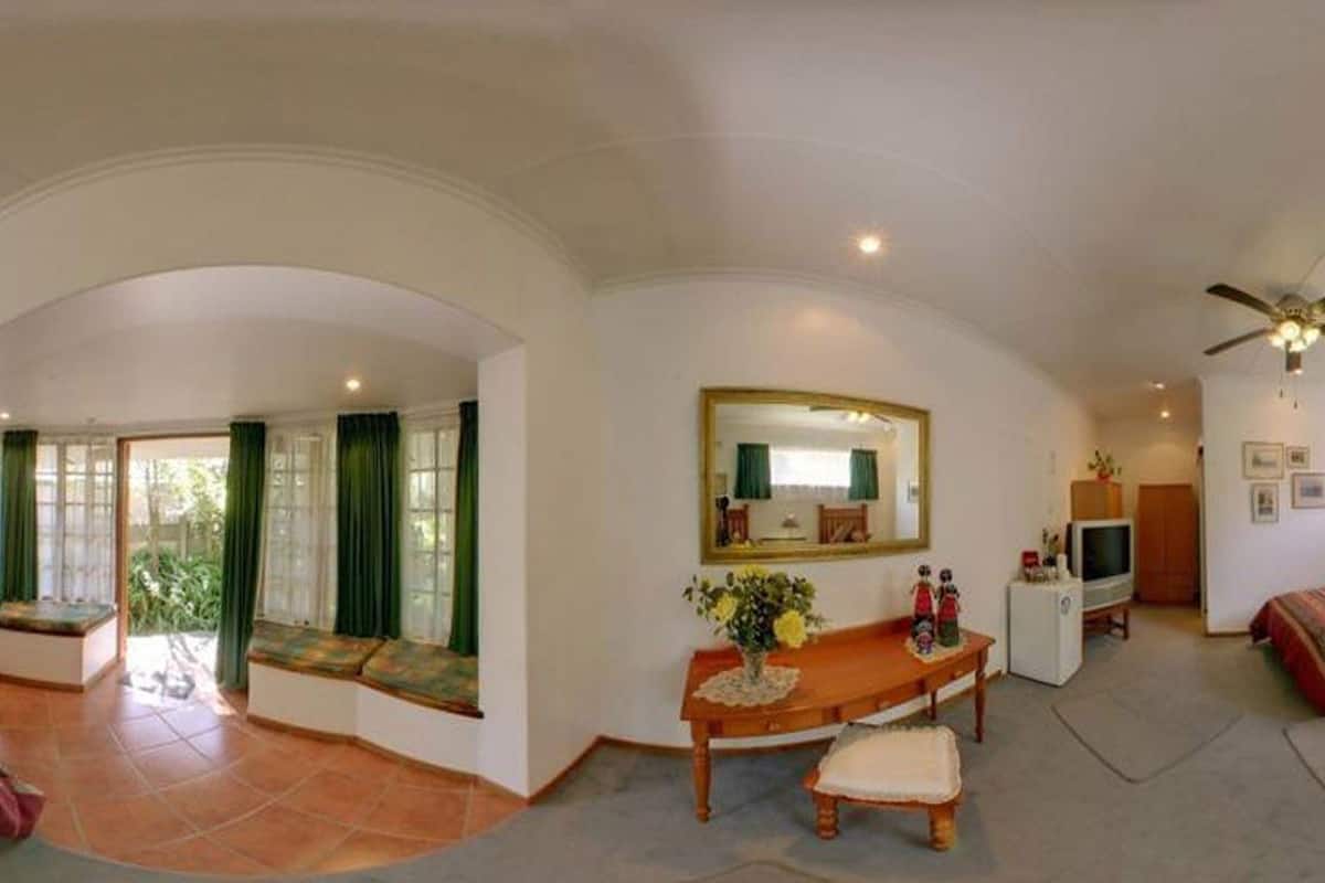 Ein geräumiges Zimmer mit gewölbter Decke, Deckenventilator, großem Spiegel, Fernseher, einem Bett mit gemusterten Betttextilien und einem kleinen Tisch mit Blumenvase.