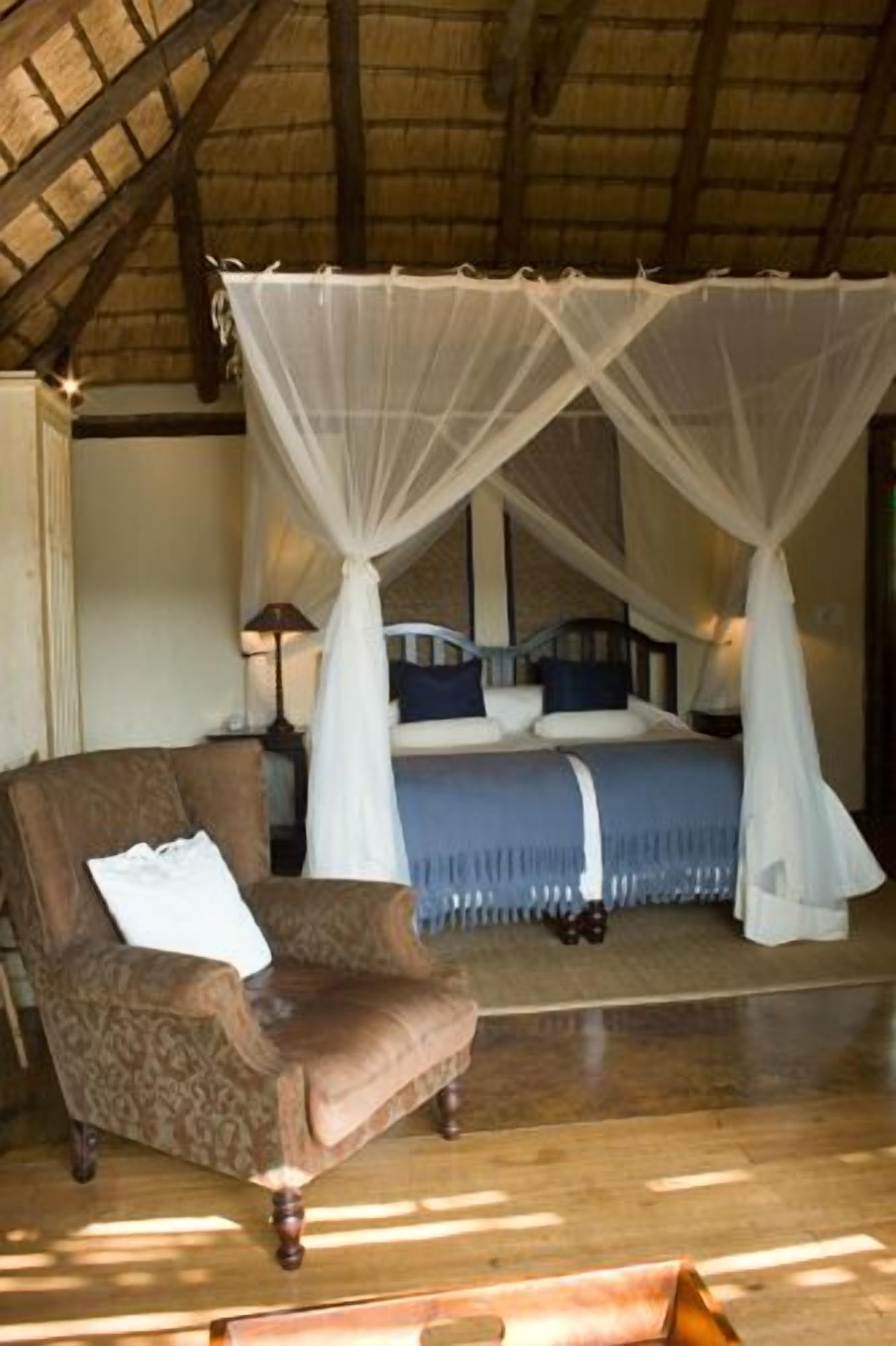 A bedroom with a canopy bed, a chair, and a bedside table.