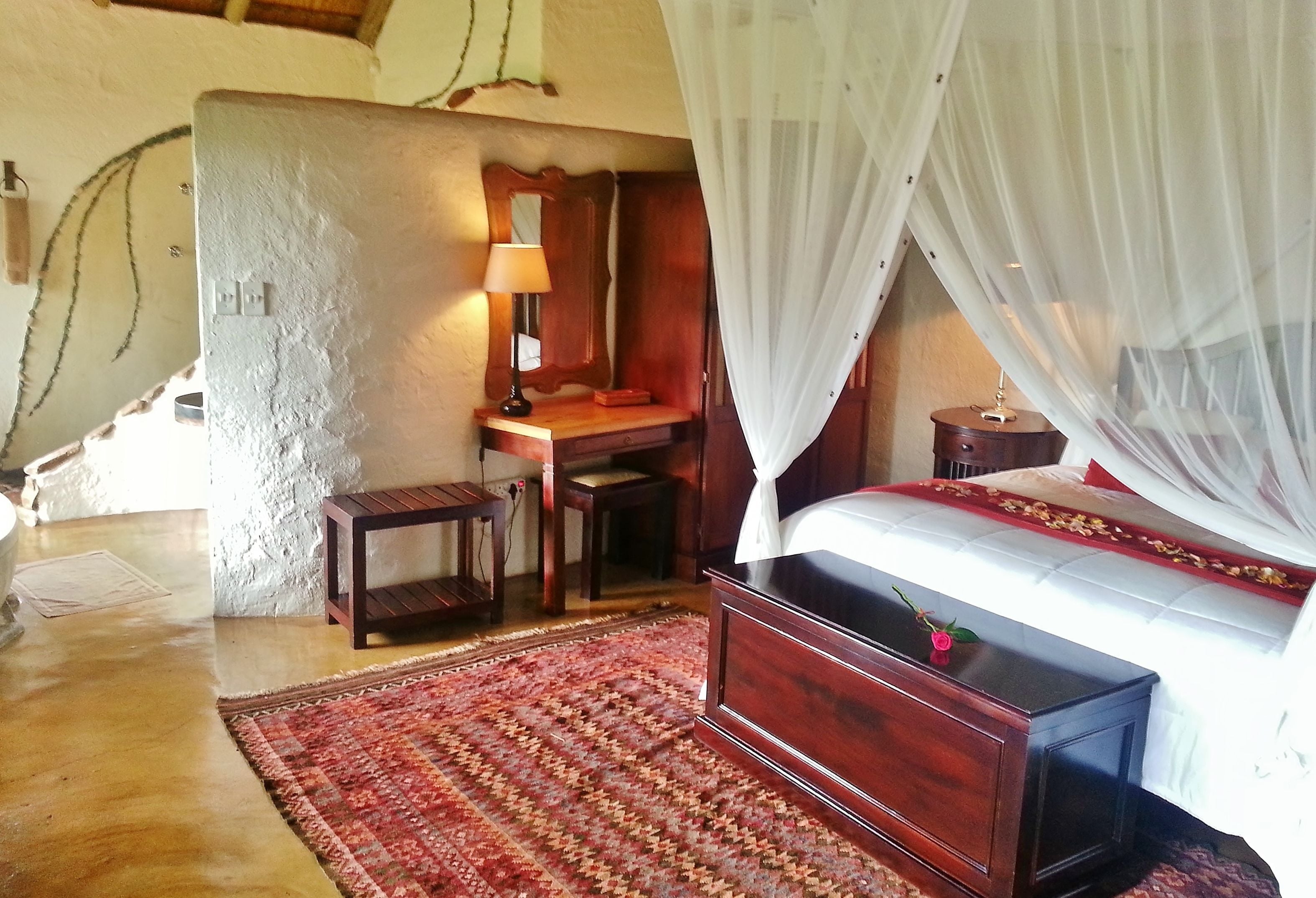 A bedroom with a bed, bedside table, lamp, and a desk with a chair.