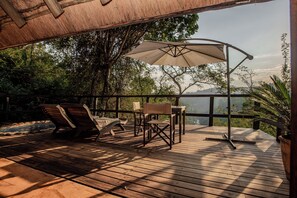 A wooden deck with lounge chairs and a table under a canopy, surrounded by trees and overlooking a landscape. - Tanamera Lodge (Sabie)