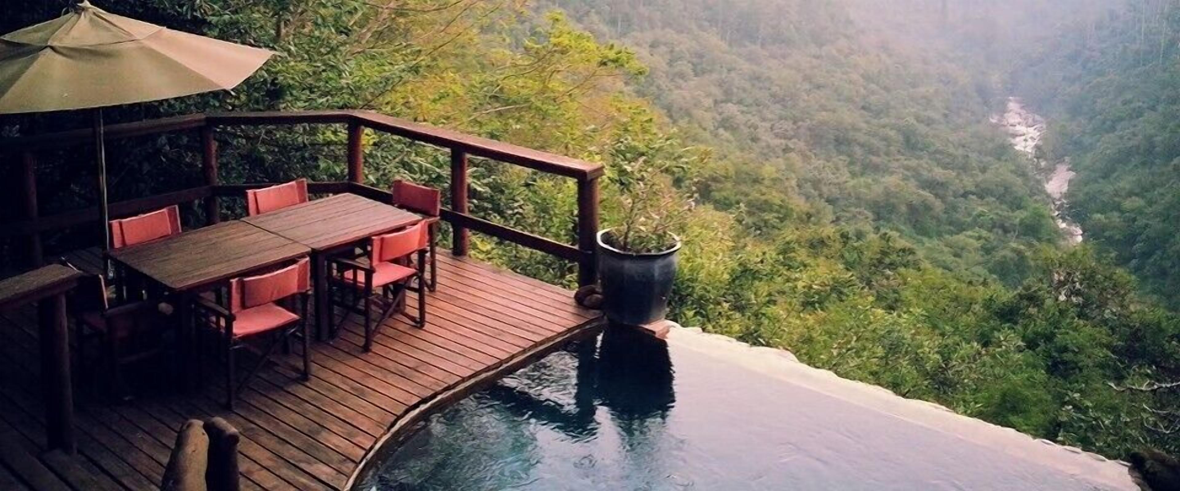 A wooden deck with a table and chairs overlooking a lush valley.
