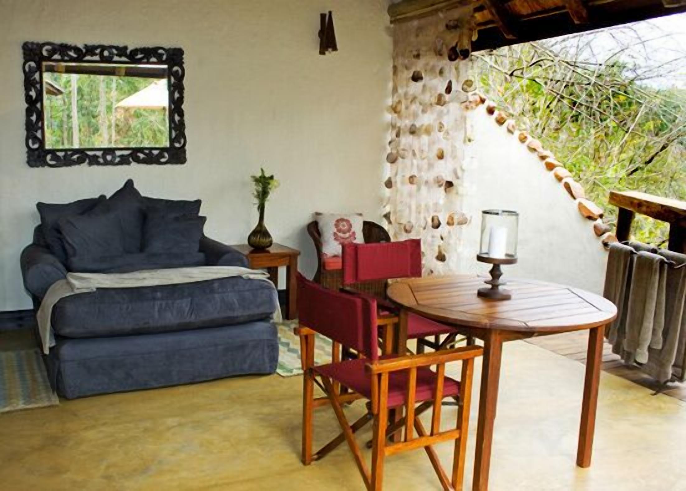 Un dormitorio con cama, una mesa con sillas, un espejo y vistas a la vegetación exterior.