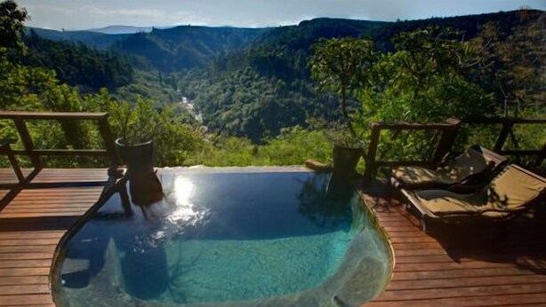 A clear view of a swimming pool with a wooden deck and lounge chairs, overlooking a mountainous landscape. - Tanamera Lodge (Sabie)
