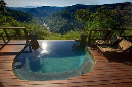 A clear view of a swimming pool with a wooden deck and lounge chairs, overlooking a mountainous landscape.