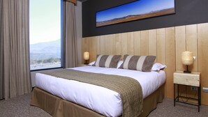 A hotel room with a large bed, a view of the mountains, a flat-screen TV on the wall, and a bedside lamp.
