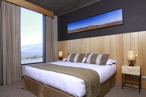 Una habitación de hotel con una cama grande, vistas a las montañas, un televisor de pantalla plana en la pared y una lámpara de noche.
