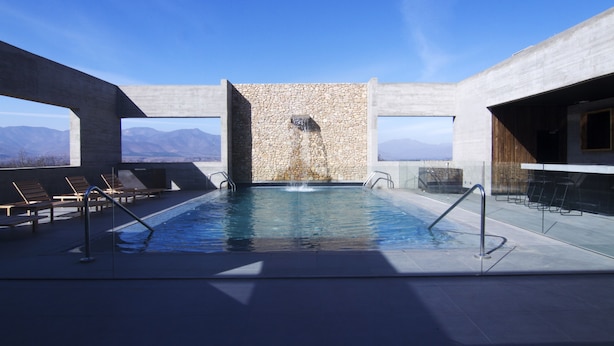 An indoor swimming pool with a stone wall and a view of mountains.