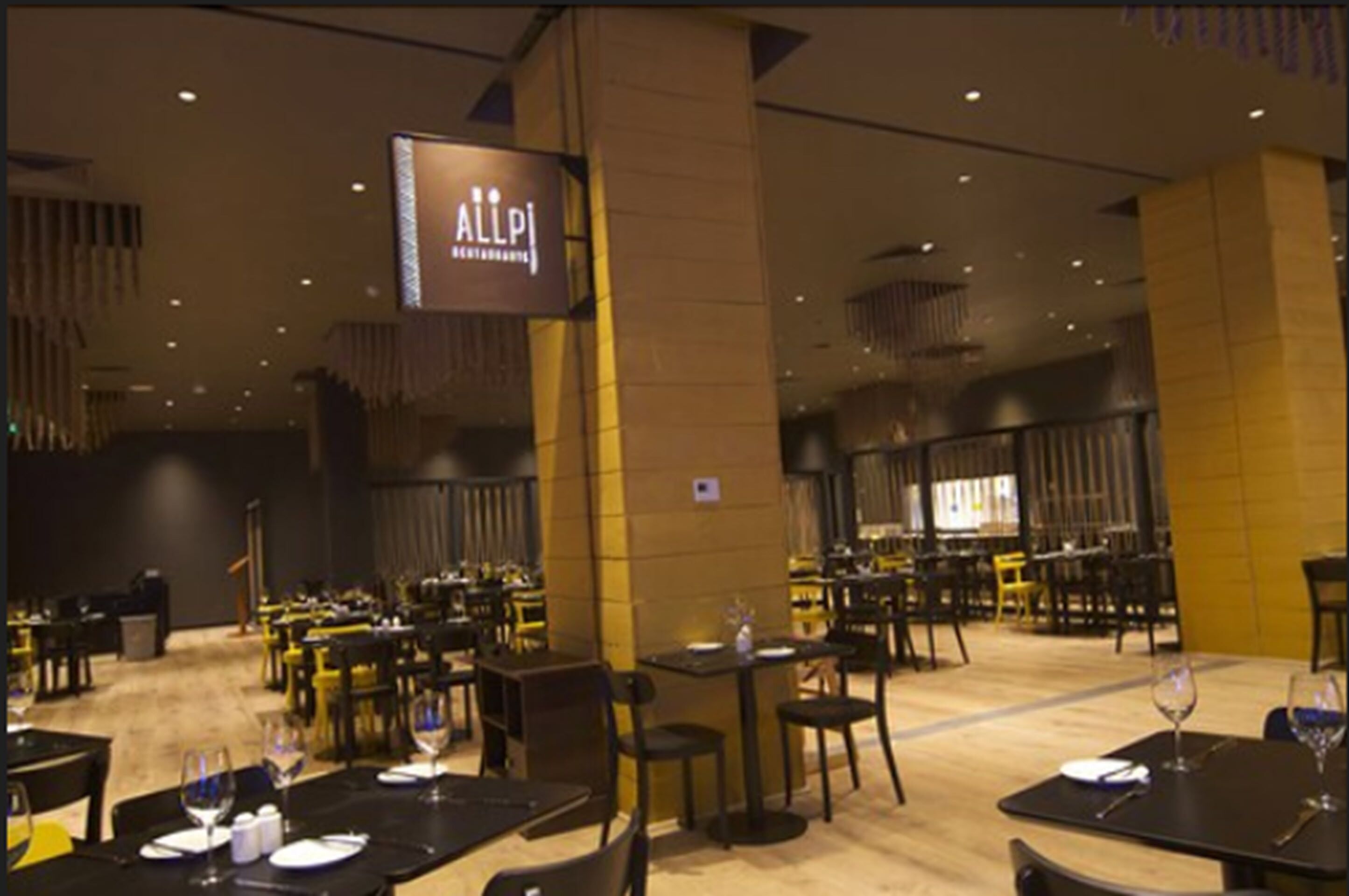 A restaurant interior with multiple tables and chairs, a large sign above the entrance, and a modern design.
