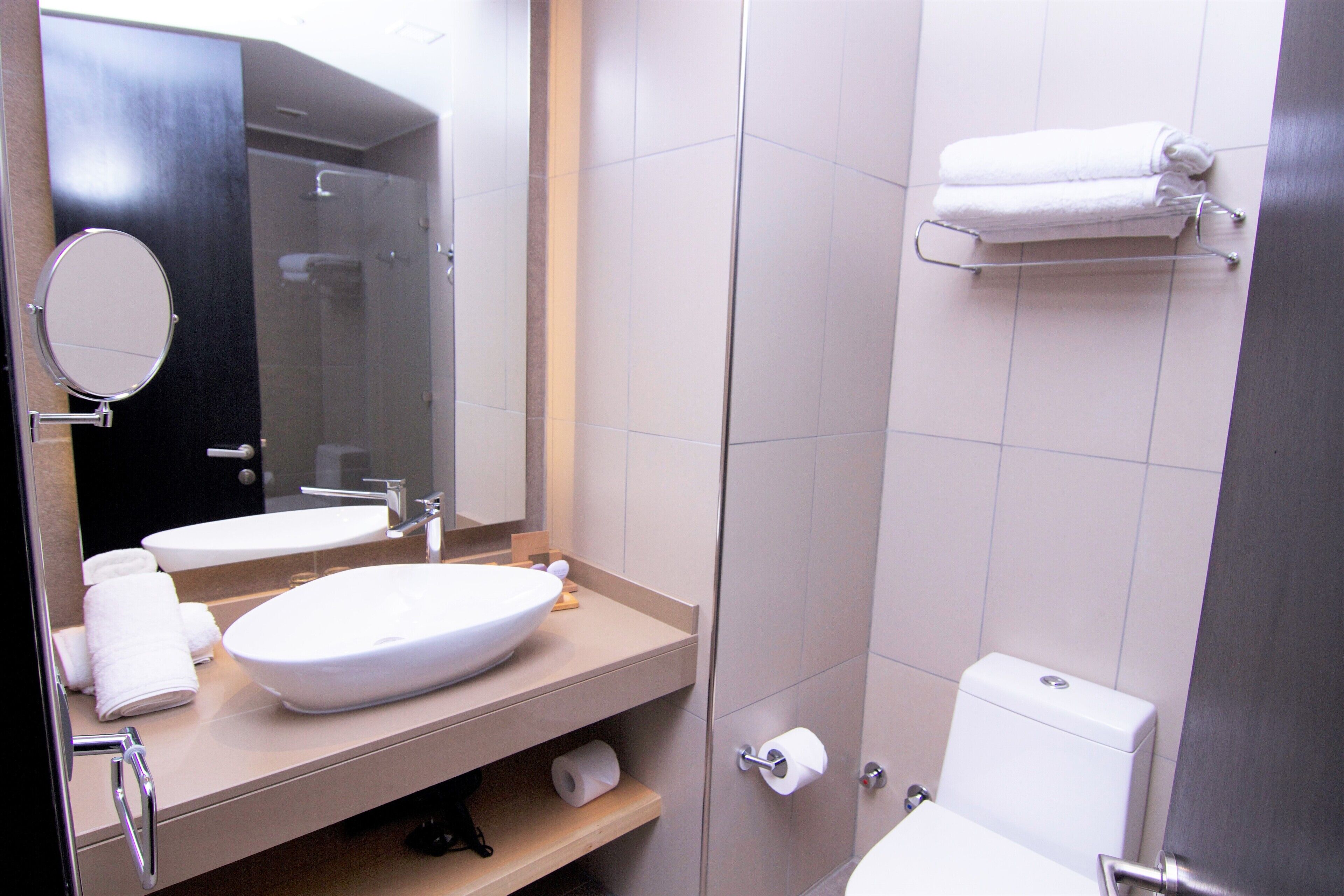 A modern bathroom with a large mirror, two sinks, a toilet, and a shower.