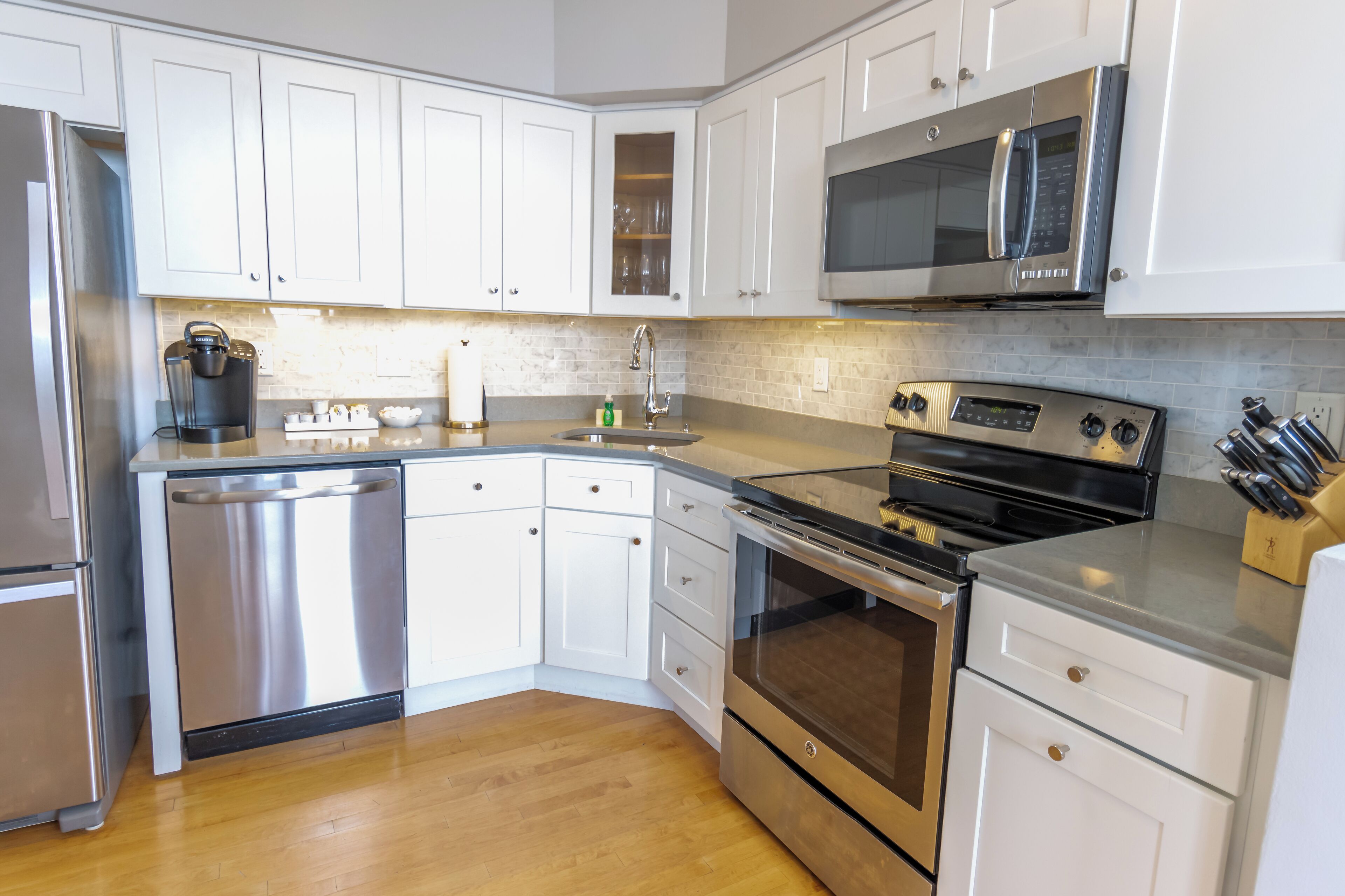 A modern kitchen with white cabinets, stainless steel appliances, and a wooden floor.