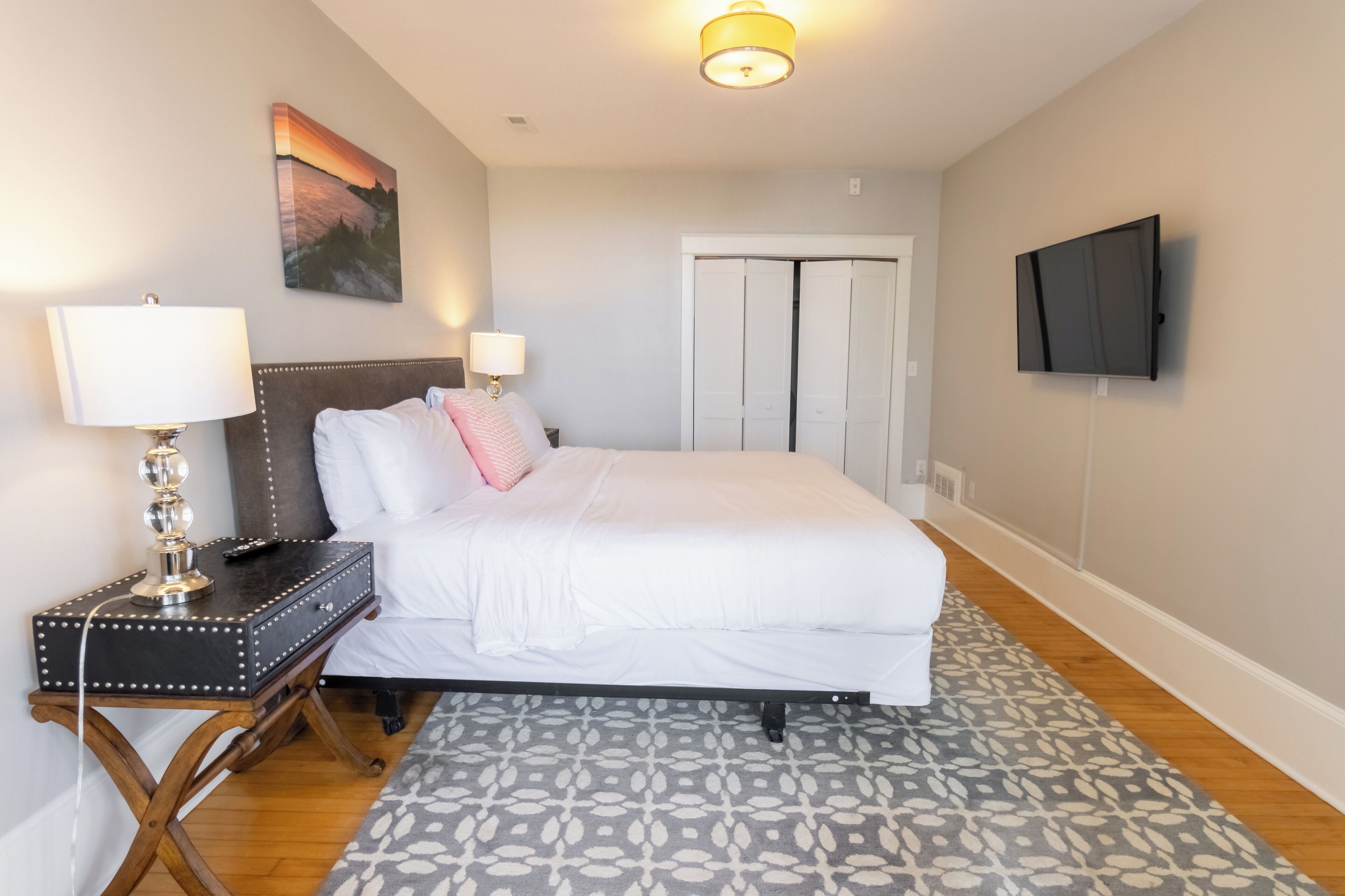 A neatly arranged bedroom with a bed, bedside lamps, a flat-screen TV, and a door with a closet.
