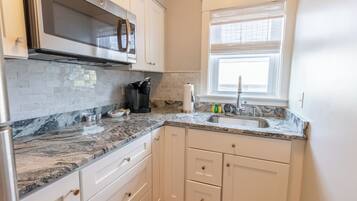 A kitchen with white cabinets, a granite countertop, a stainless steel sink, and a window with blinds.