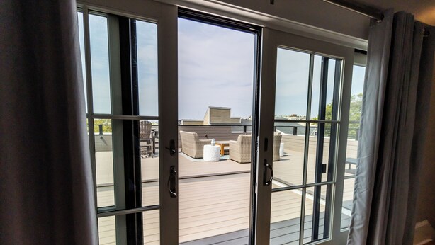 Eine Glastür öffnet sich zu einer Terrasse mit Korbmöbeln und Blick zum Himmel.