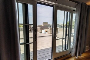 Une porte-fenêtre coulissante donne sur une terrasse extérieure aménagée avec des meubles en osier et offre une vue sur le ciel.