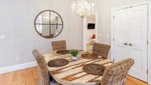 A dining area with a round table, wicker chairs, a chandelier, and a large mirror on the wall. - The Newport Lofts - 359 Thames Street (Newport)