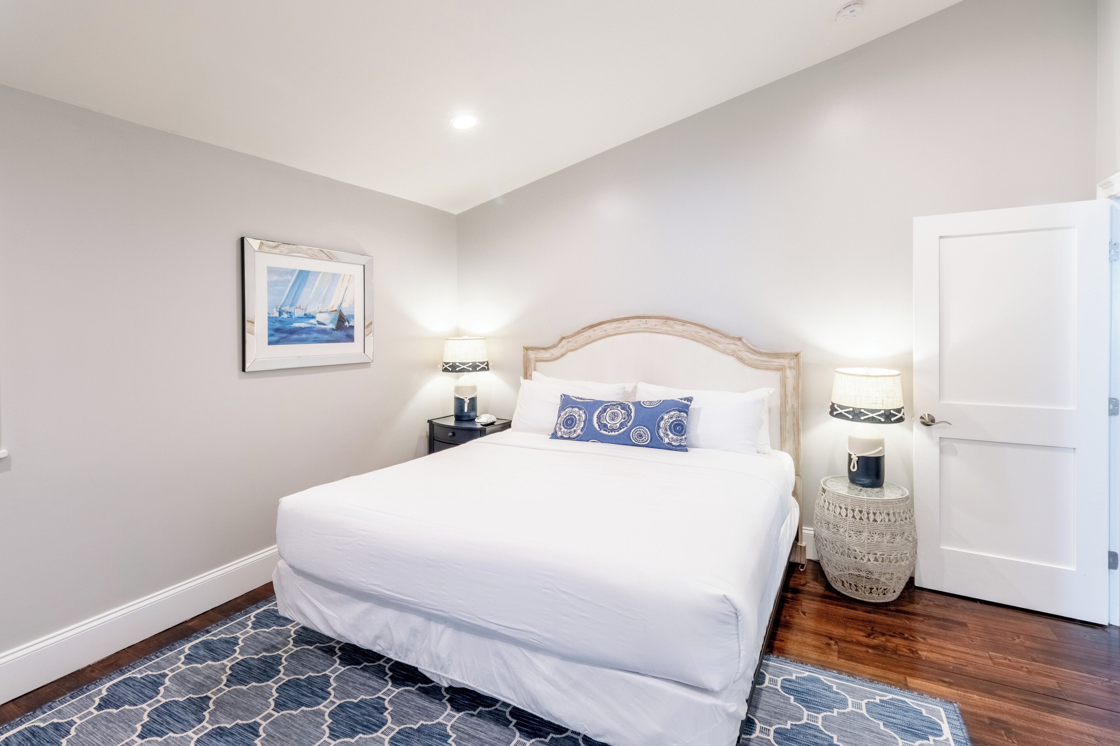 A neatly arranged bedroom with a large bed, two bedside tables with lamps, a framed picture on the wall, and a door.