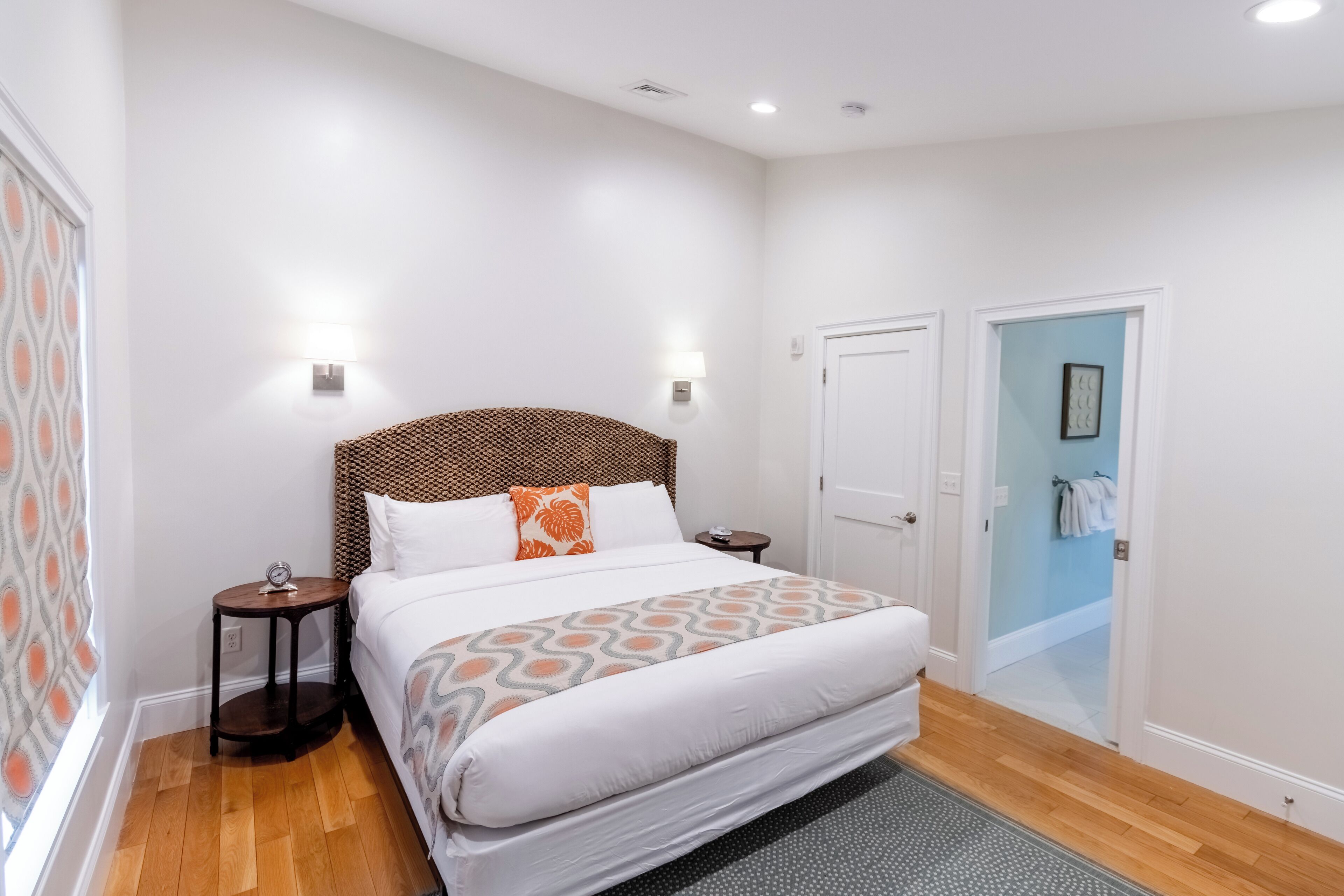 A hotel room with a large bed, two bedside tables, a headboard, and a door leading to a bathroom.