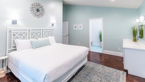 A bedroom with a large bed, a decorative wall piece, a small bedside table, and a nightstand. - The Newport Lofts - 359 Thames Street (Newport)