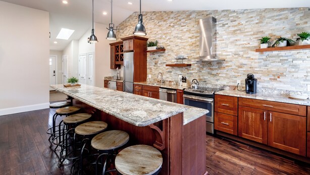 A modern kitchen with a stone backsplash, wooden cabinets, and a bar area with stools. - The Newport Lofts - 359 Thames Street (Newport)