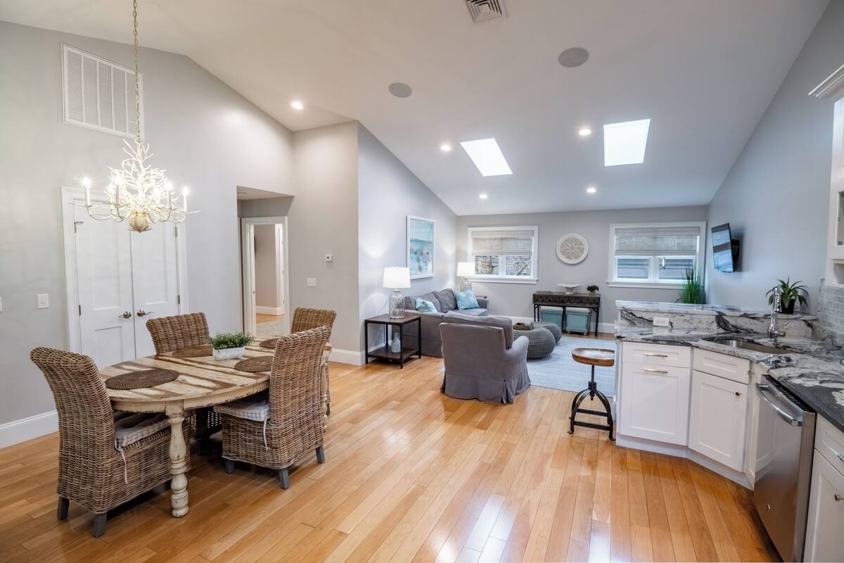 A spacious living area with a dining table, wicker chairs, a sofa, and a kitchen with white cabinets and a marble countertop.