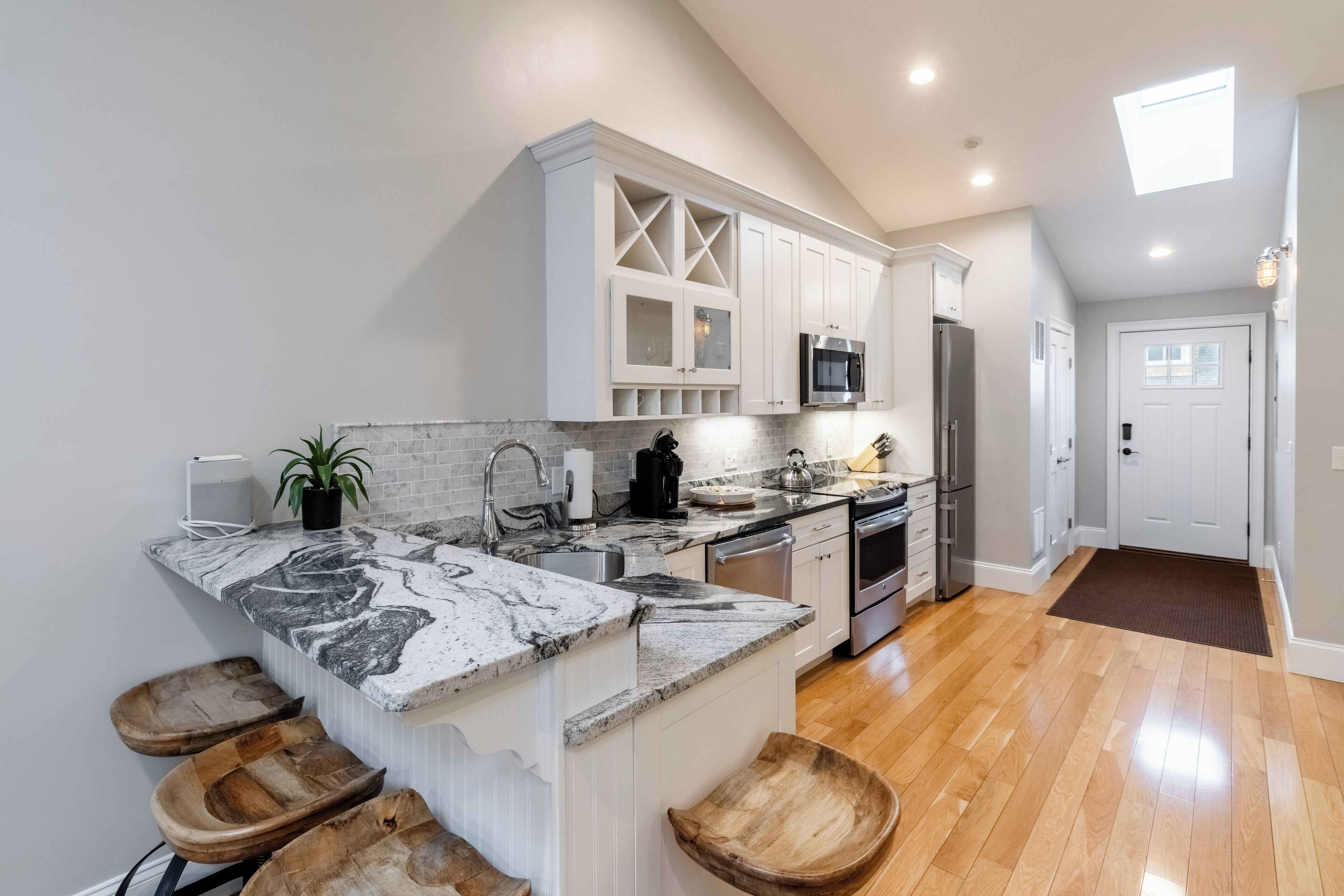 A modern kitchen with white cabinets, a marble countertop, wooden stools, and a built-in oven.