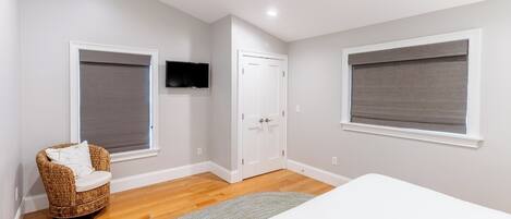 A bedroom with a bed, a wicker chair, a television, and a door.