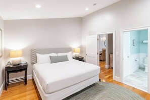 A bedroom with a large bed, bedside tables with lamps, a patterned headboard, and a view into the bathroom. - The Newport Lofts - 359 Thames Street (Newport)
