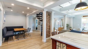 Amplia sala de estar con una mesa de comedor de madera, un sofá oscuro y una zona de cocina con encimera de mármol.