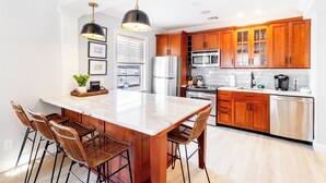 Una cocina moderna con una isla central, armarios de madera, electrodomésticos de acero inoxidable y una lámpara colgante.