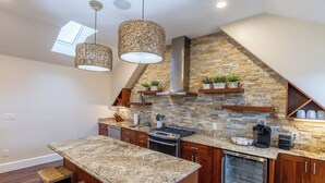 Una cocina con salpicadero de piedra, armarios de madera, estufa integrada y luces colgantes.