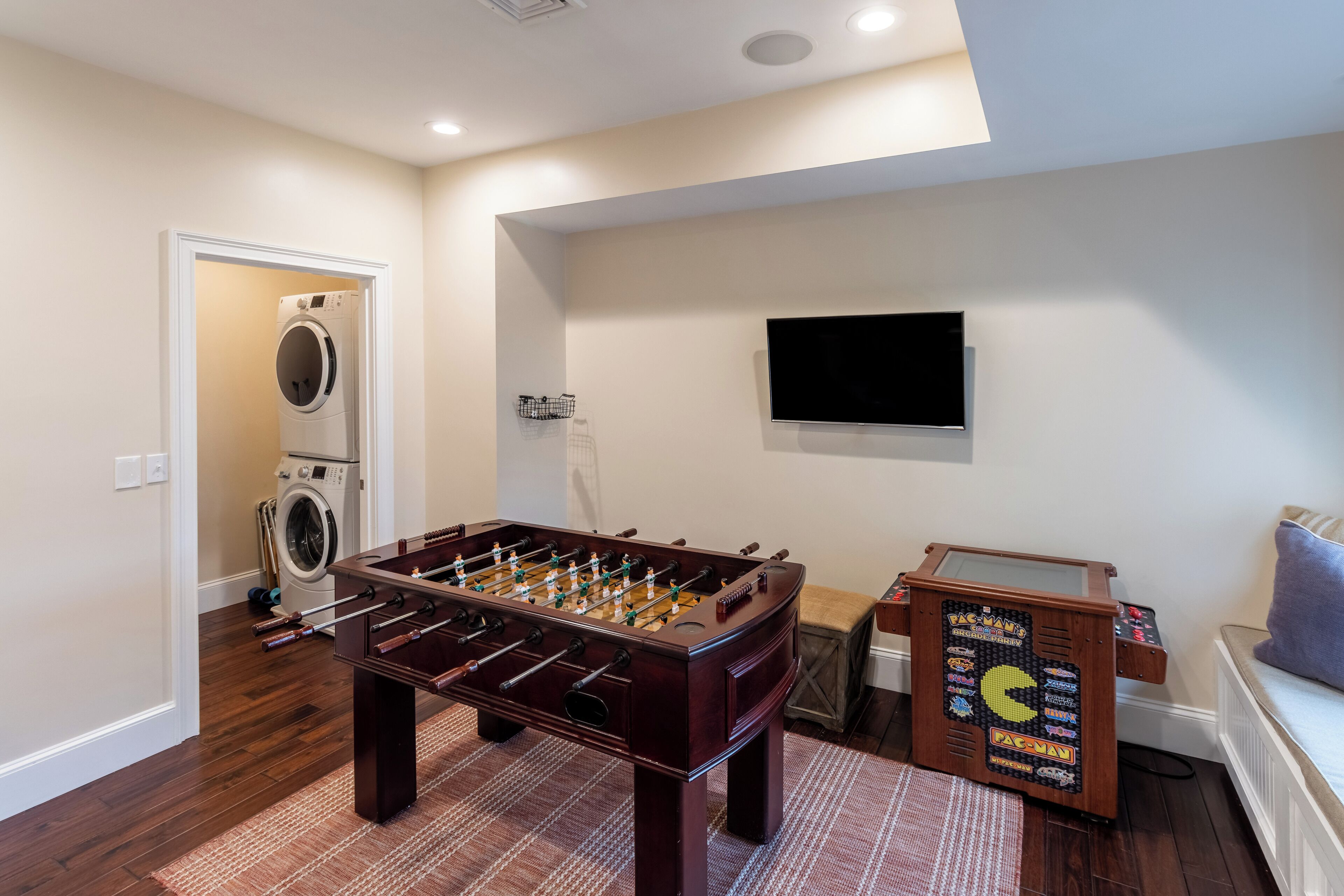 A room with a foosball table, a washing machine, and a television mounted on the wall.