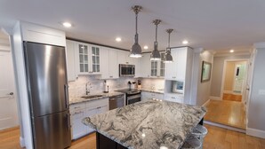 Une cuisine moderne dotée d’un grand îlot central, d’appareils électroménagers en acier inoxydable et de luminaires suspendus.
