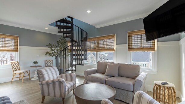 Un salon moderne avec un escalier en colimaçon, un grand canapé, des fauteuils à rayures et une table basse ronde.