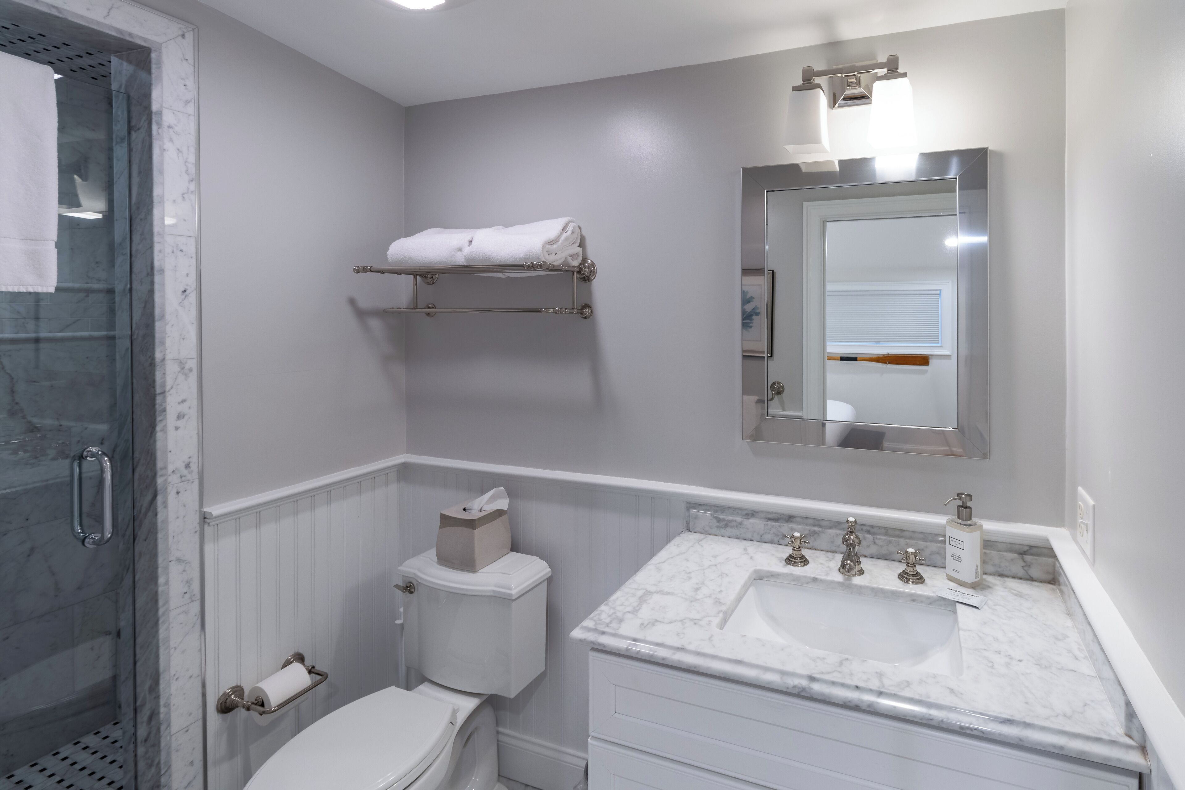 A bathroom with a glass shower enclosure, a toilet, a sink with a marble countertop, and a towel rack.