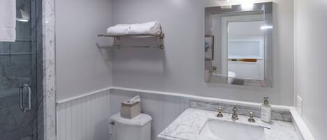 A bathroom with a glass shower enclosure, a toilet, a sink with a marble countertop, and a towel rack.
