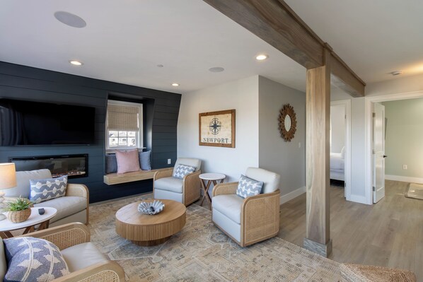 A cozy living room with a fireplace, comfortable seating, and a wall-mounted TV. - The Newport Lofts - 617 Thames Street (Newport)
