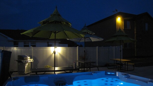Ein Whirlpool mit blauem Licht, zwei Sonnenschirme und ein Grill im Hinterhof bei Nacht.