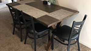 Ein Essbereich mit einem dunklen Holztisch, vier schwarzen Stühlen, einer gewebten Tischmatte, einem Topfpflanzen und einem gerahmten Schild an der Wand.