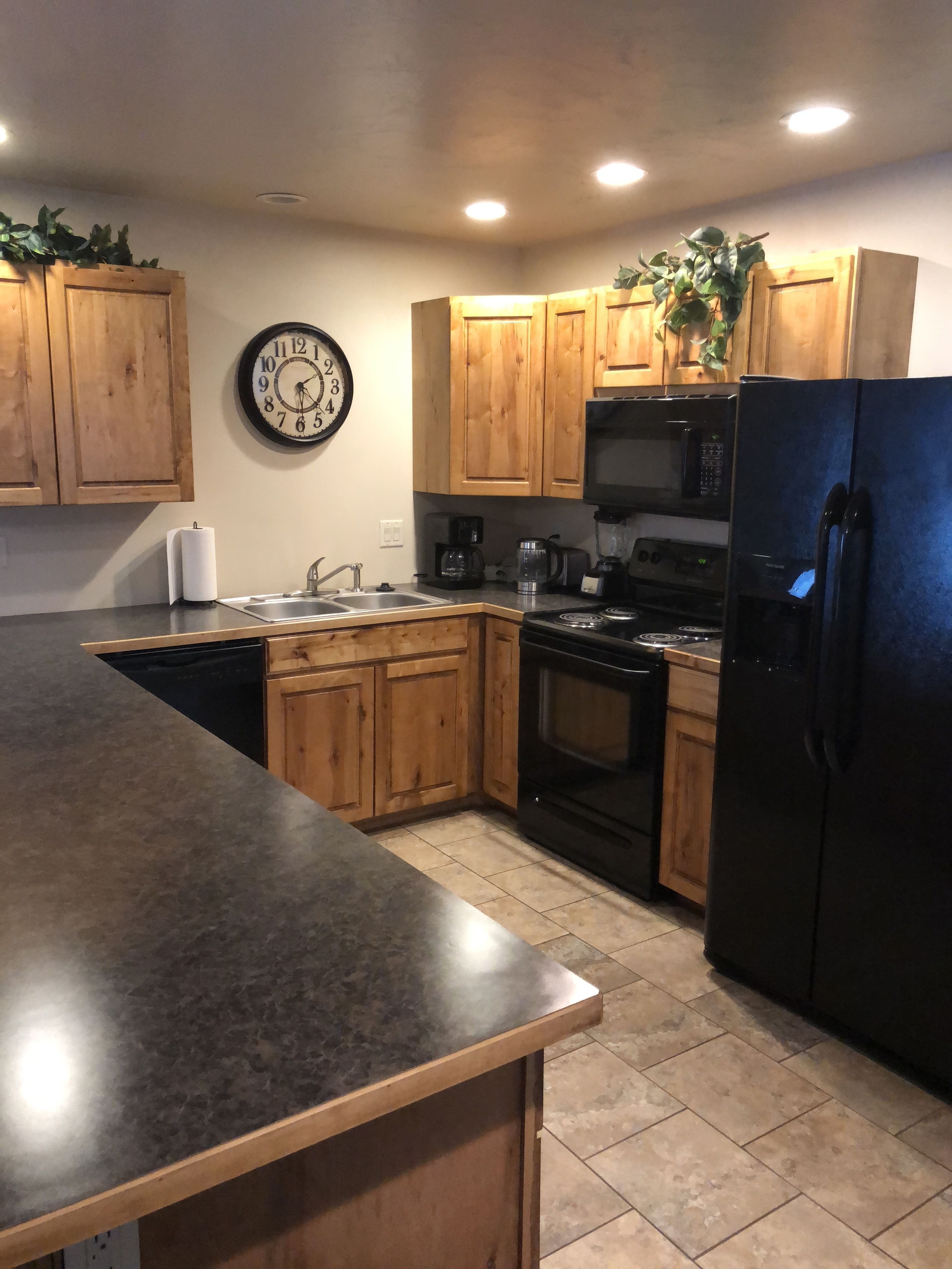A kitchen with wooden cabinets, a black refrigerator, a microwave, a stove, and a clock on the wall.