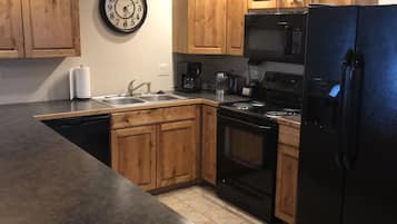 A kitchen with wooden cabinets, a black refrigerator, a microwave, a stove, and a clock on the wall.