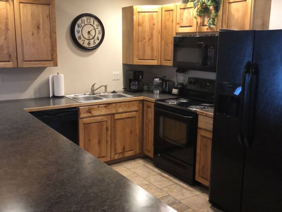 A kitchen with wooden cabinets, a black refrigerator, a microwave, a stove, and a clock on the wall.